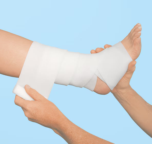 White ankle support bandage being wrapped around a person's ankle by two hands, shown against a solid light blue background.