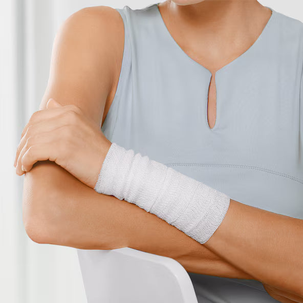 Person wearing a light gray sleeveless top with a white arm bandage on a neutral background